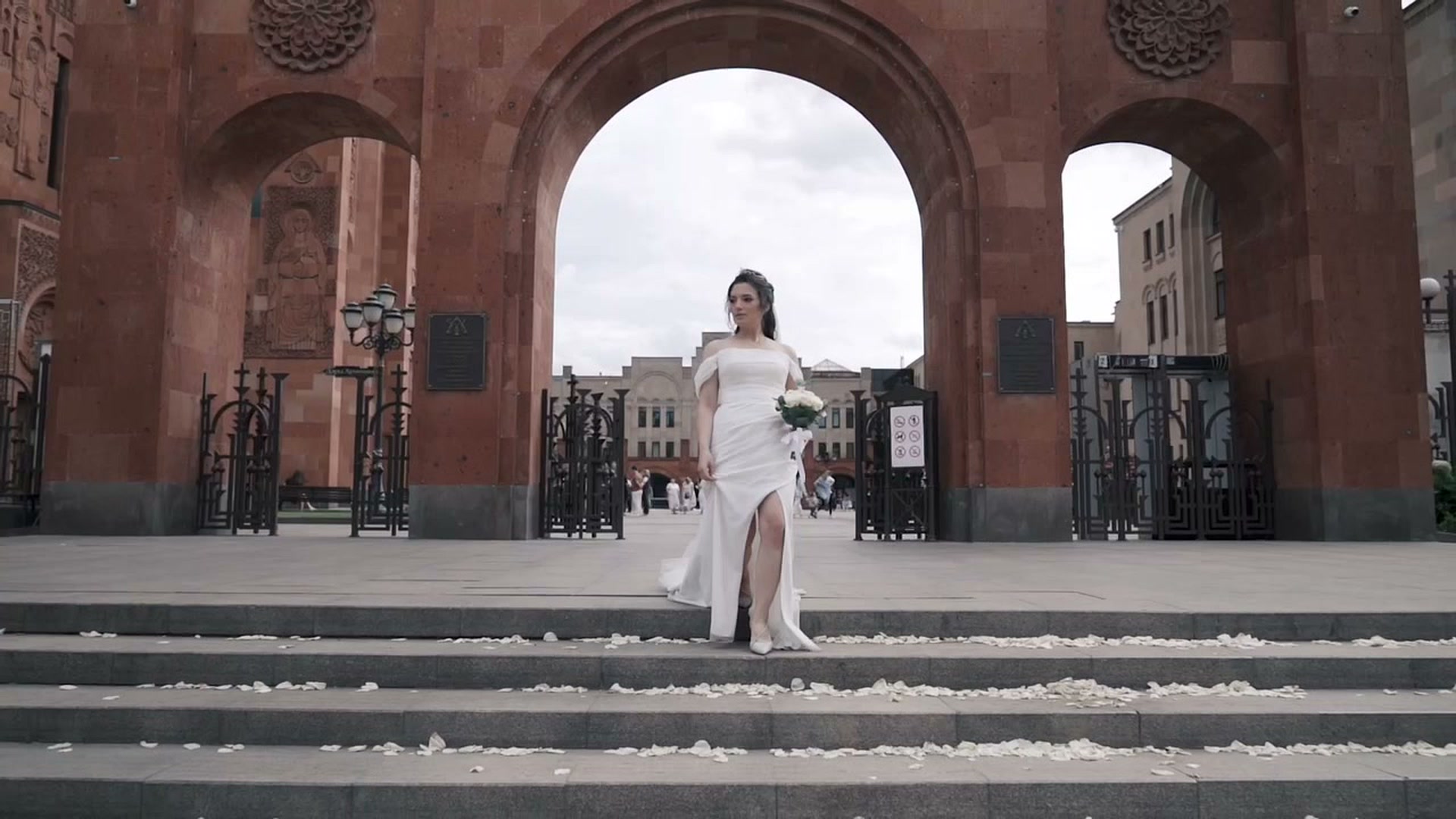 Невеста с букетом спускается по ступеням у городской арки.